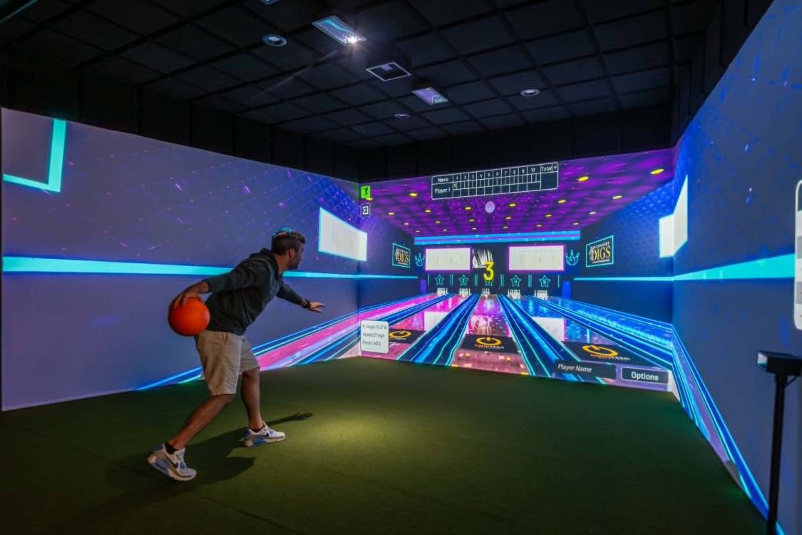 Player bowling in a projection-based bowling simulator room with colour-changing lighting